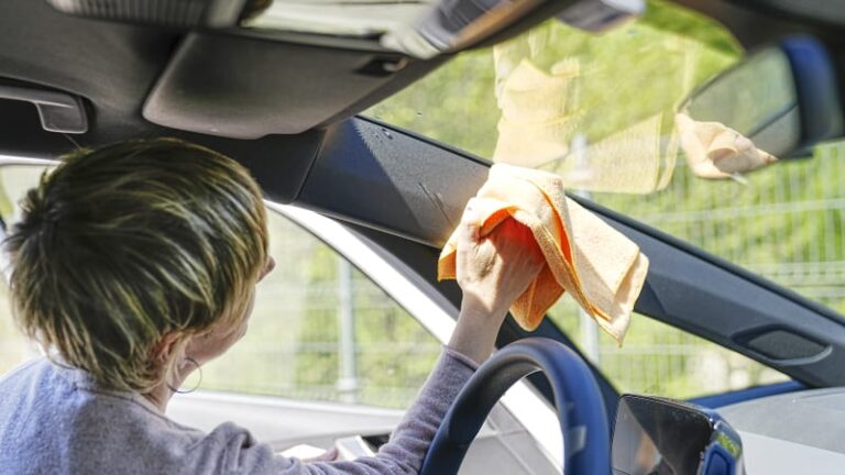 woman cleaning inside of car windshield at a sunny service area